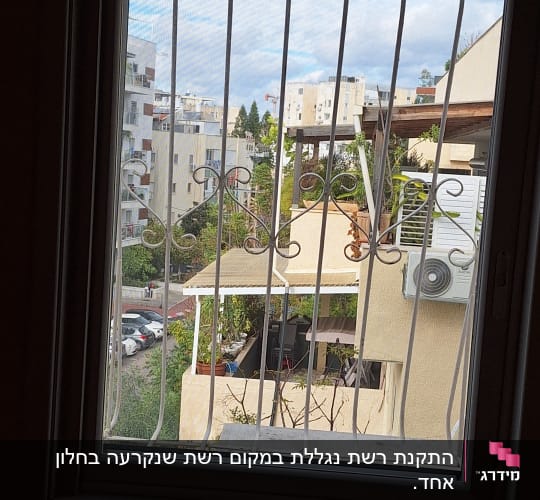 חלון עם סורגים ונוף של בניינים ועצים